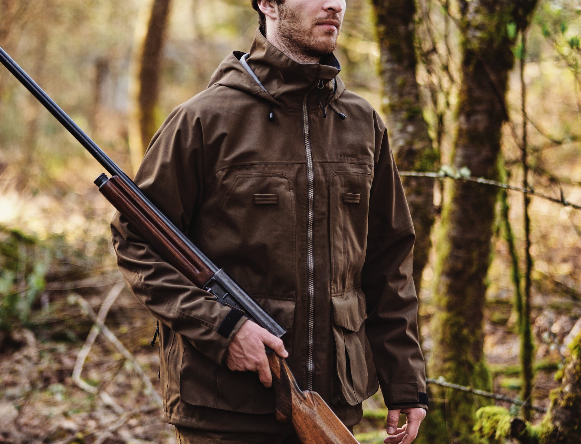 Hunter holding a rifle in the woods wearing a Filson 3-Layer Field Jacket