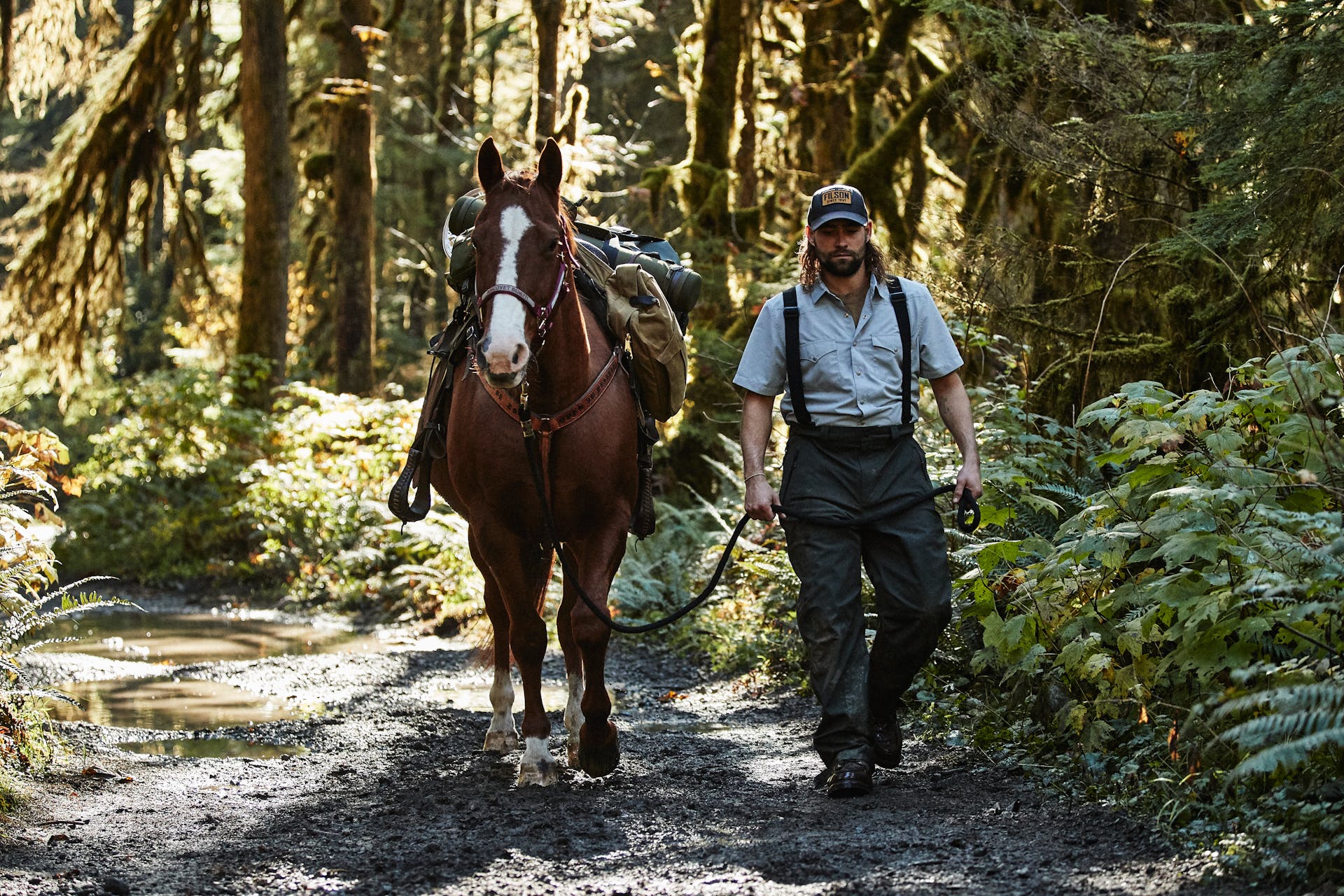 Man wearing Filson Skagit Rain Pants in peat guiding horse along dirt trail