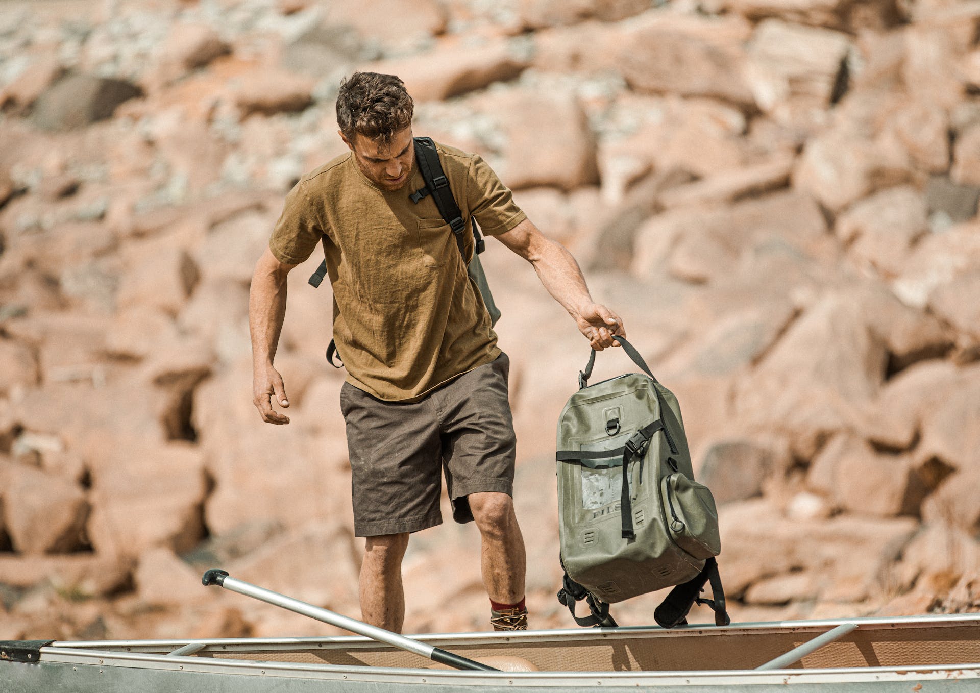 Man carrying a Filson Backpack Dry Bag in green into a canoe on a sunny day