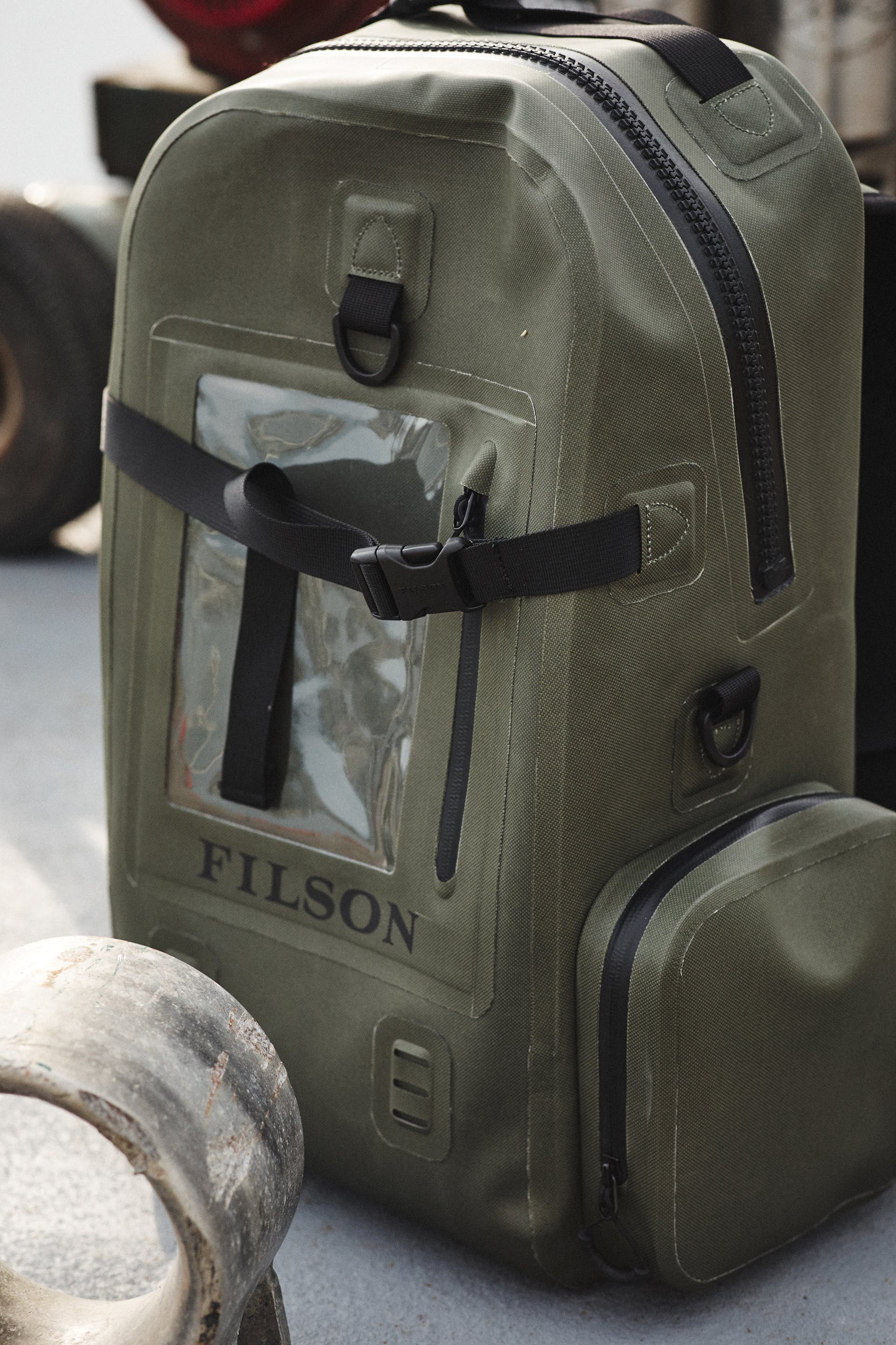 Filson Backpack Dry Bag in green sitting upright on a dock next to an engine