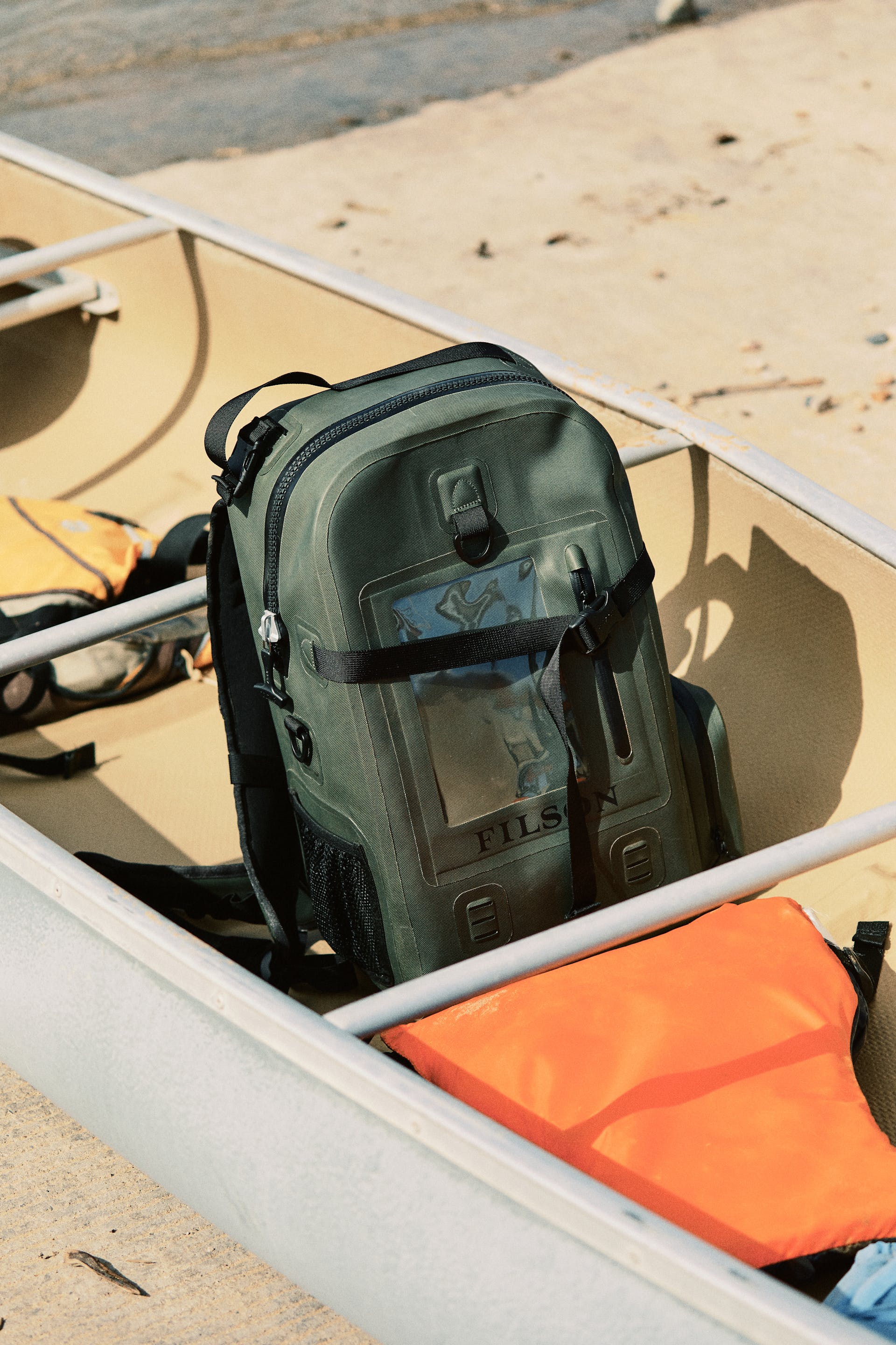 Filson Backpack Dry Bag in green sitting in a canoe on the shore of a lake