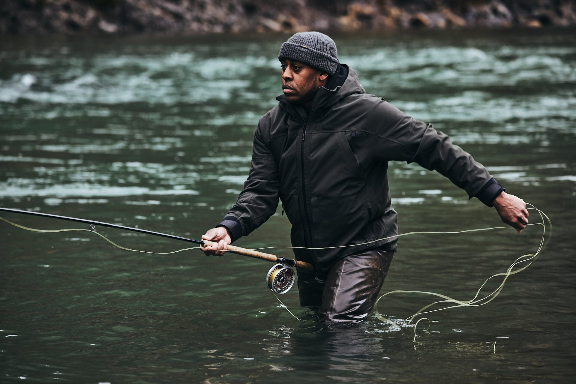 Man wearing Filson Skagit Rain Jacket in peat wading in water while pulling in fishing line