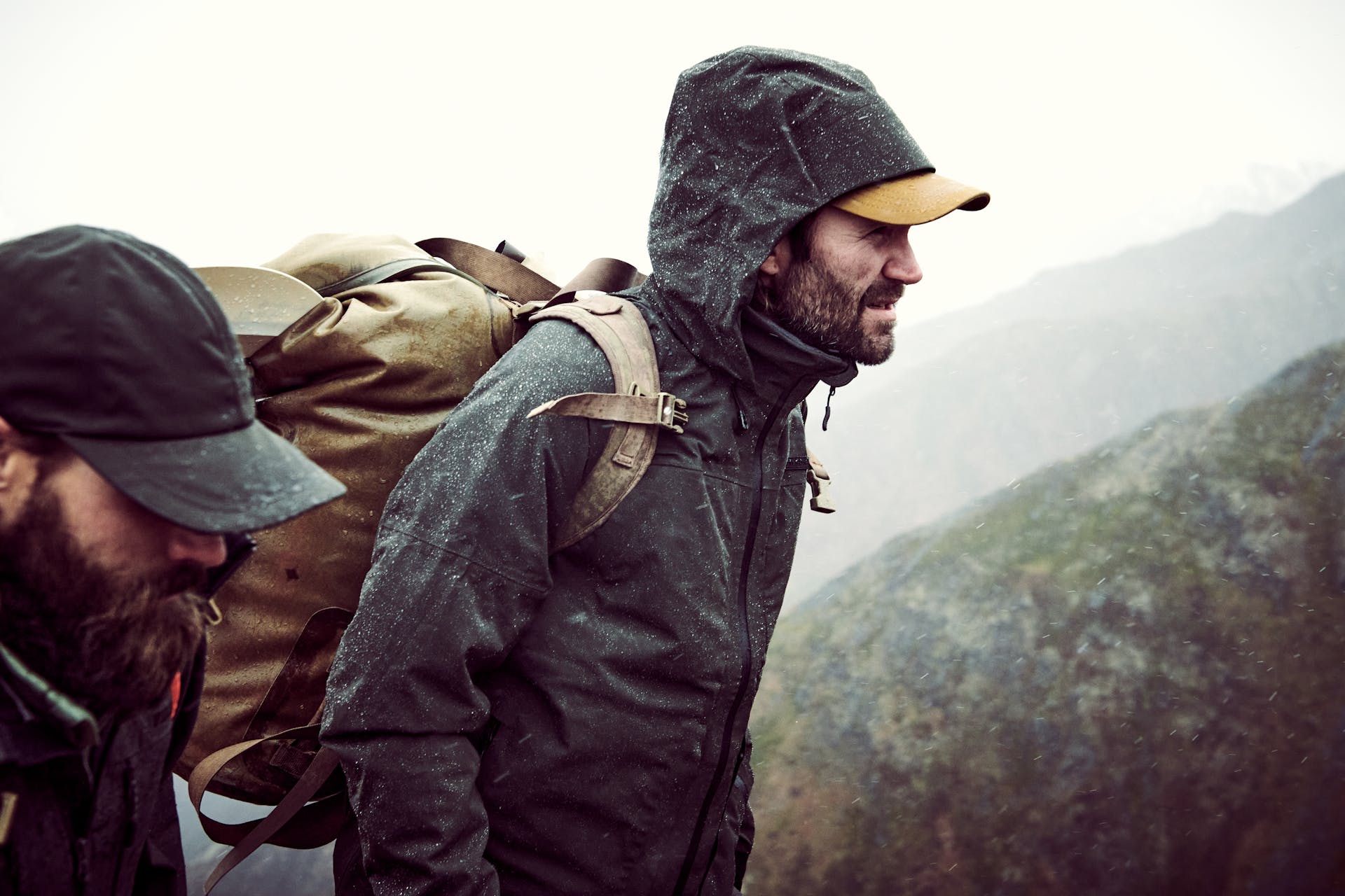 Man wearing Filson Skagit Rain Jacket in peat looking ahead while hiking alongside another gentleman