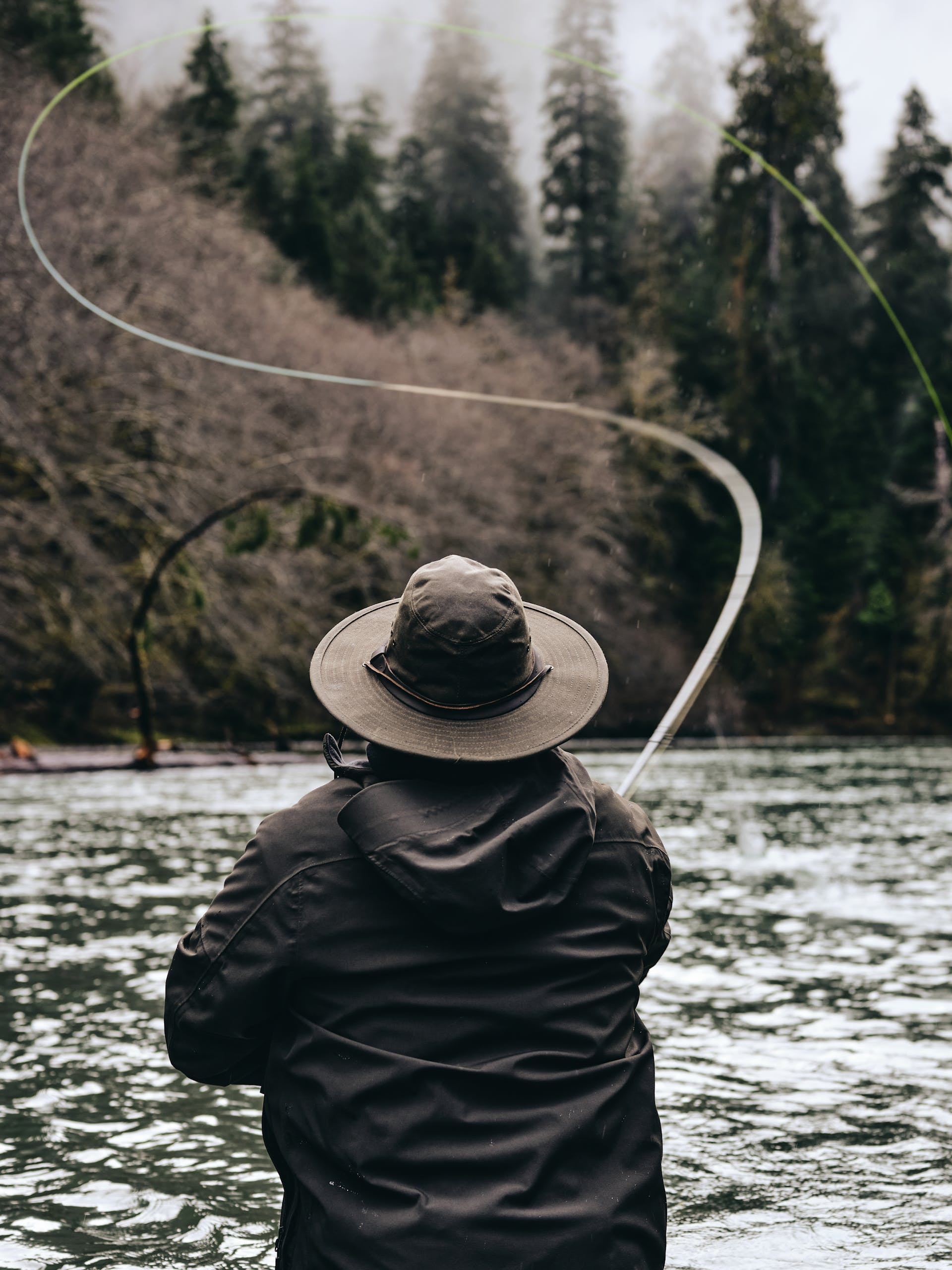 Man wearing Filson Skating Rain Jacket in peat casting a fishing line while wading in water