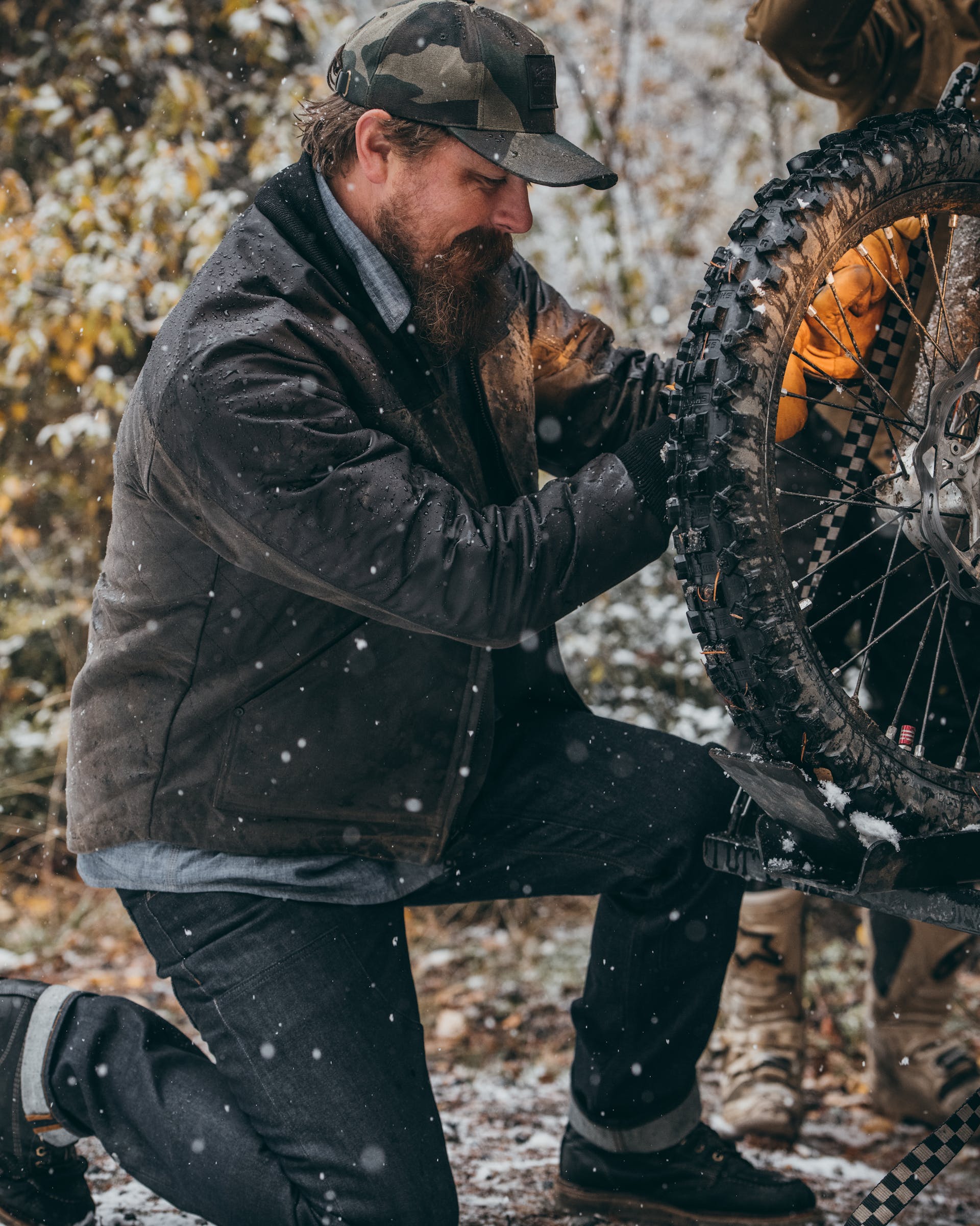 Man wearing Filson Alcan Quilted Jacket in cinder  kneeling and fixing the wheel on a motorcycle