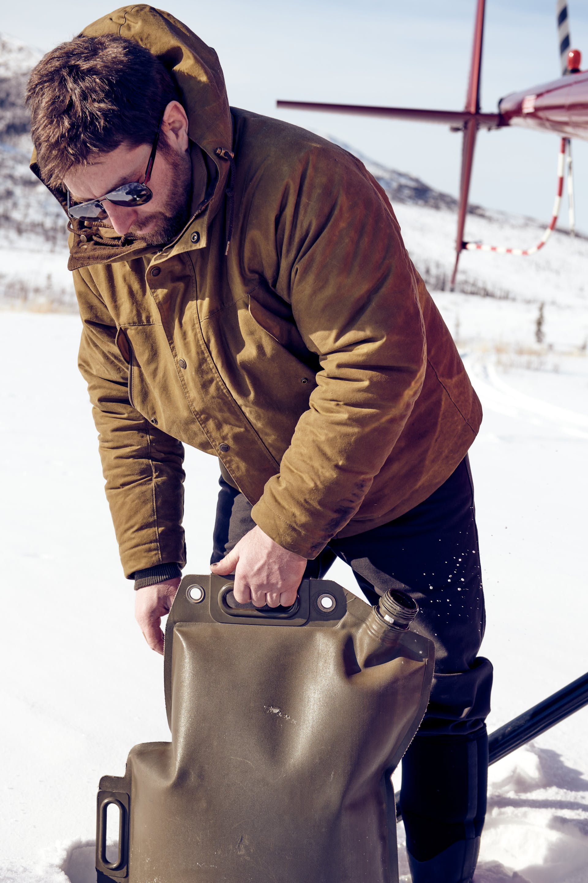 Man carrying a water container in the snow wearing a Filson Insulated Shelter Cloth Parka