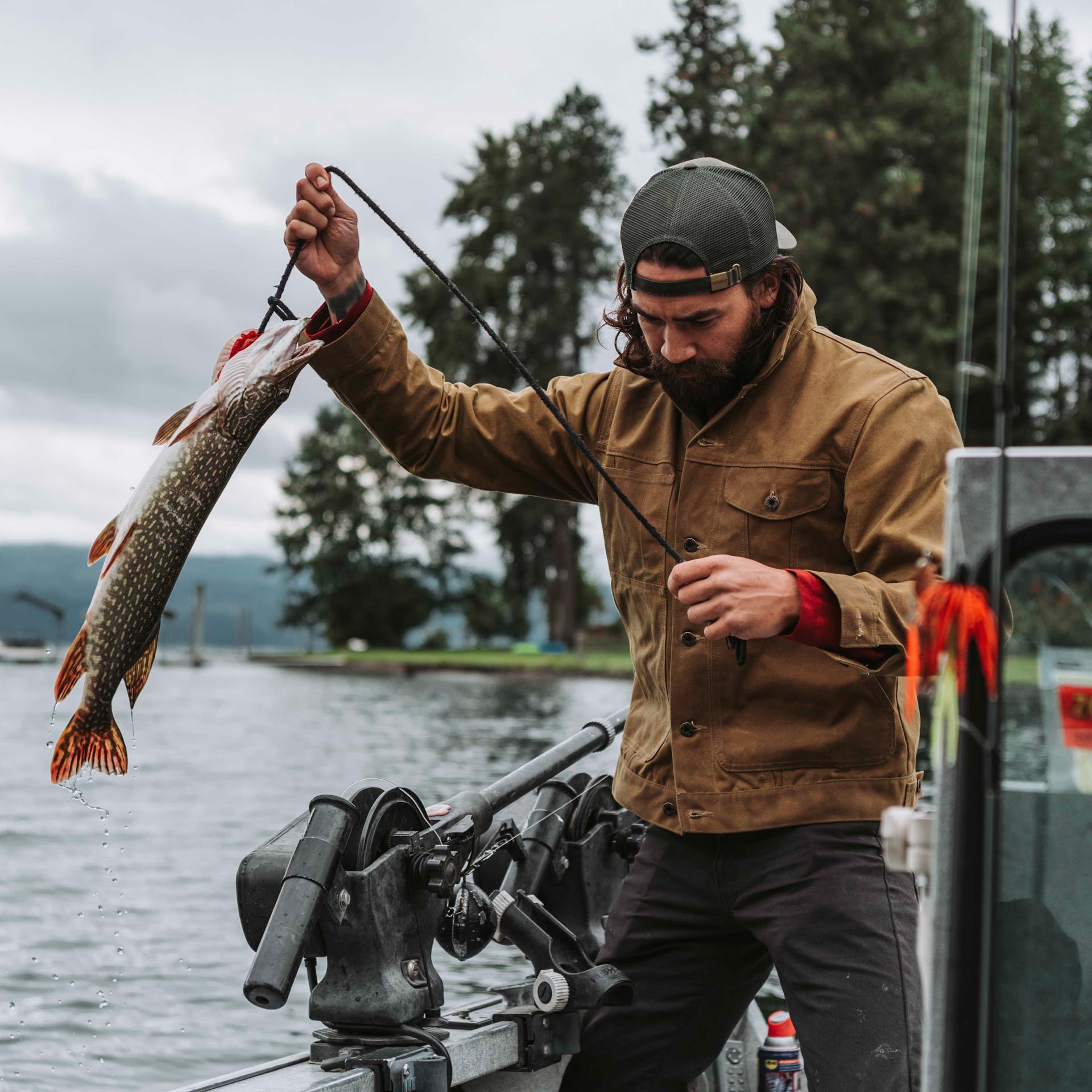Man holding a fish on a line on a boat while wearing a Filson Tin Cloth Short Lined Cruiser Jacket in dark tan.