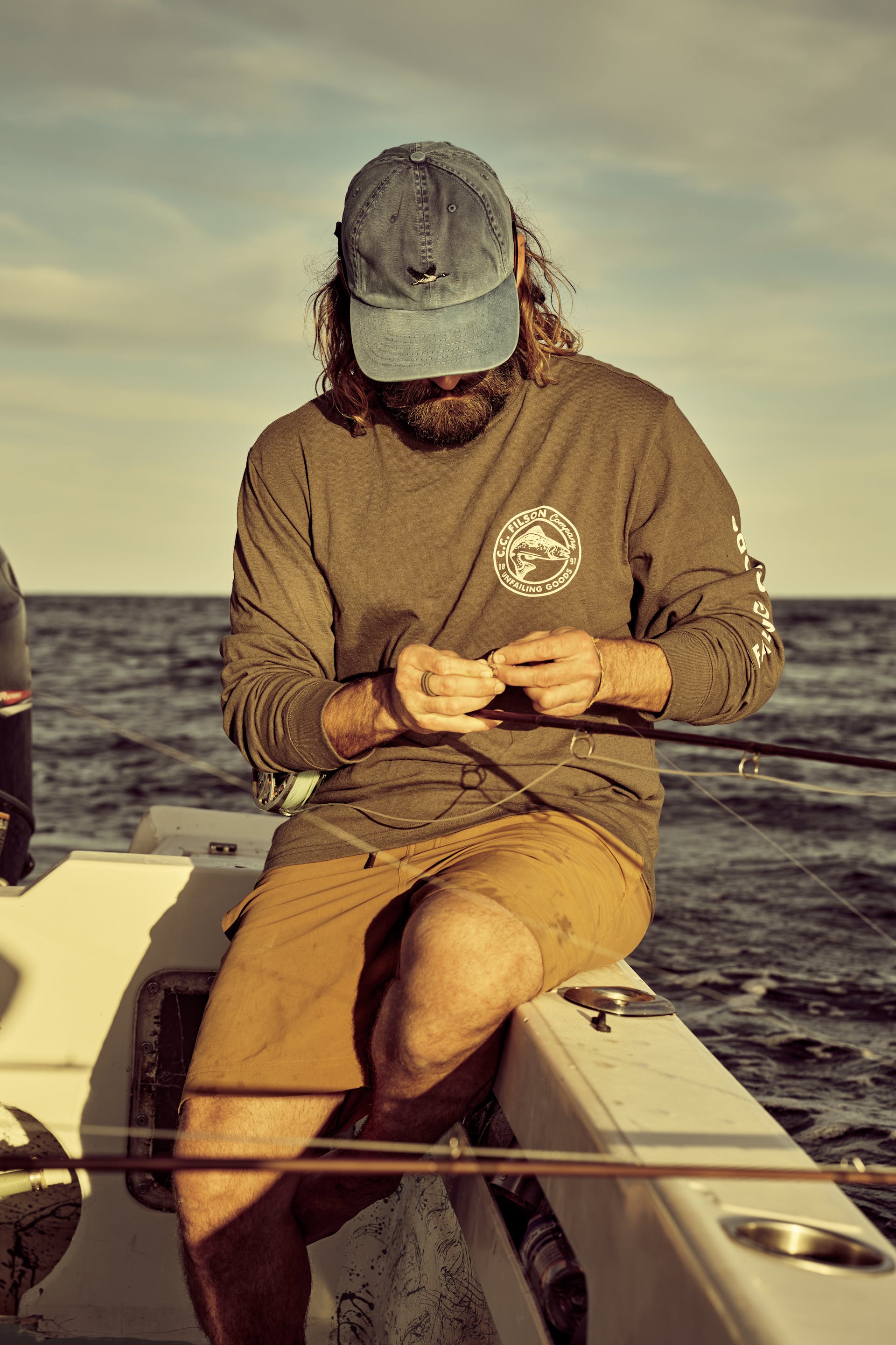 Man rigging a fly fishing rod on a boat wearing a Filson Long Sleeve Pioneer Graphic T-Shirt